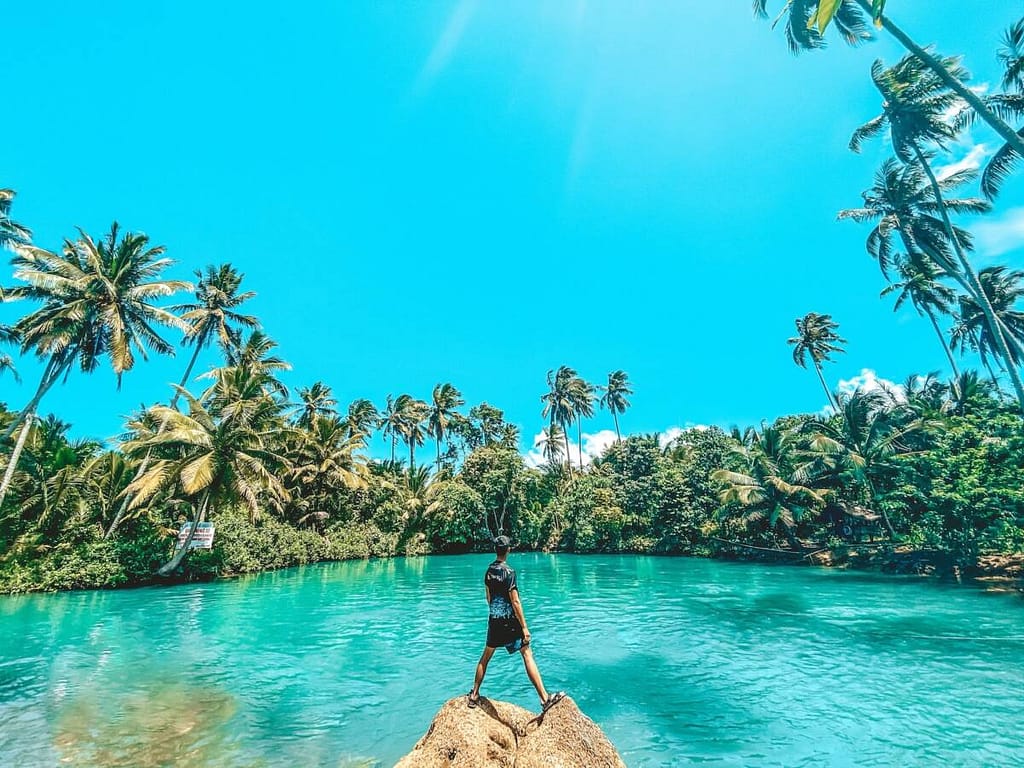 woman in black dress standing on rock near body of water during daytime